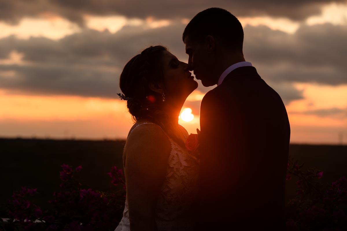 Newlyweds kiss - backlit by spectacular sunset