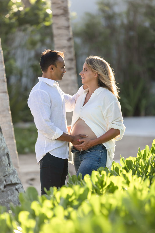 Expecting couple embrace under palm tree