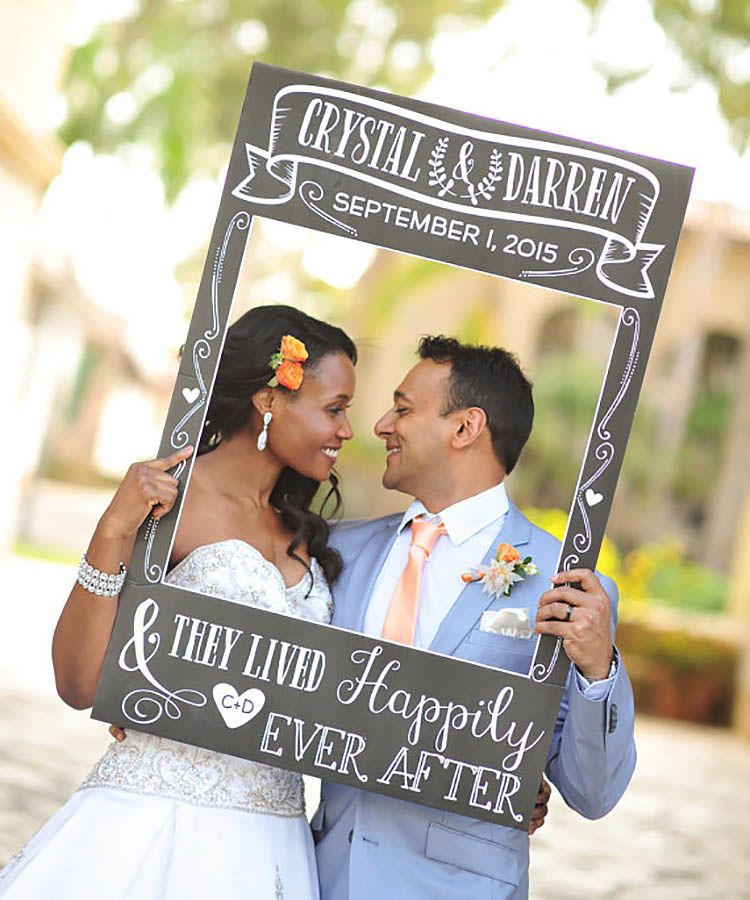 newlyweds pose behind picture frame with their details