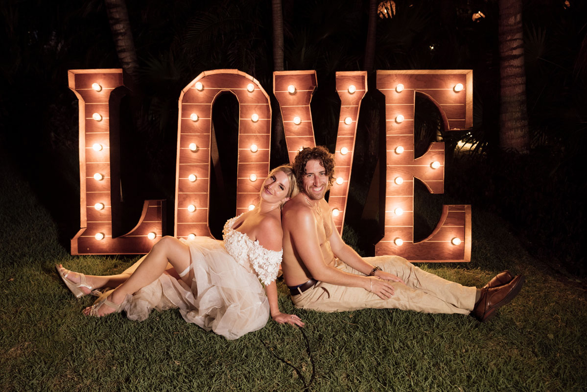 Newlyweds pose in front of neon Love sign