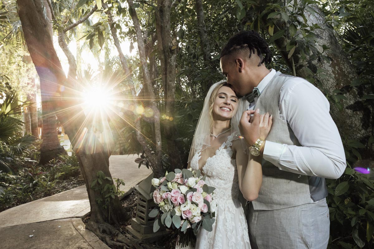 Newlywed husband kisses his bride, lit by a sparkling sunset