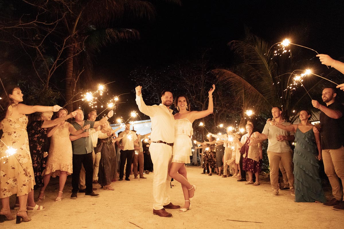 Cheering newlyweds embrace under a gauntlet of sparklers