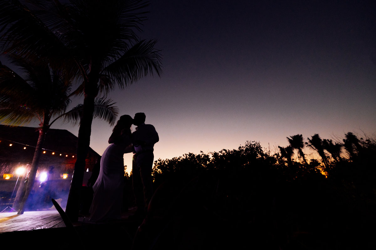 Newlyweds kiss silhouetted by stunning sunset