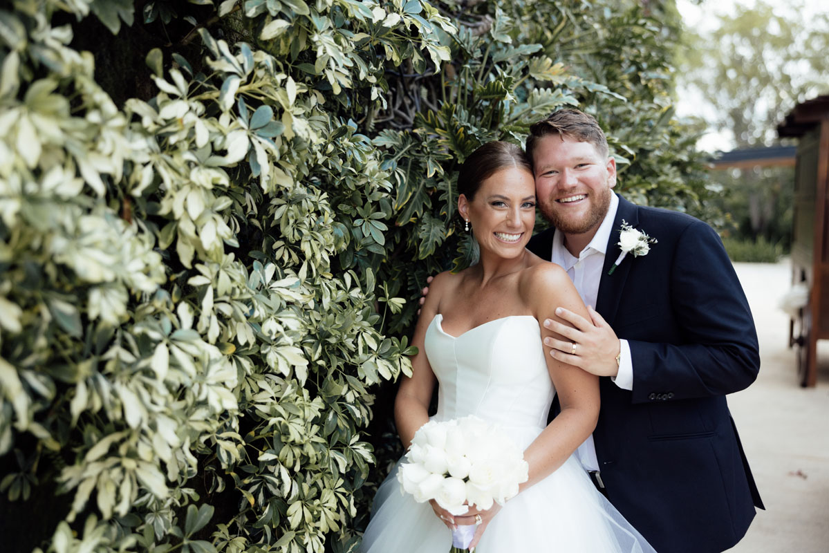 Beaming newlyweds pose by tropical bushes