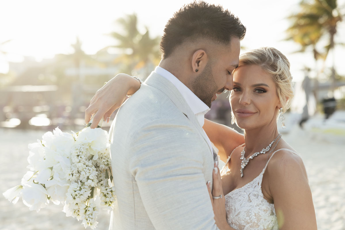 Newlyweds embrace on the beach backlit by misty sunlight