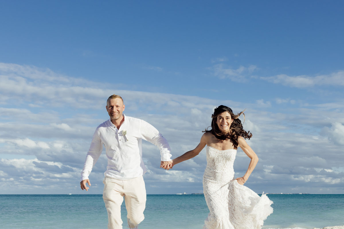 Laughing newlyweds run on the beach hand in hand