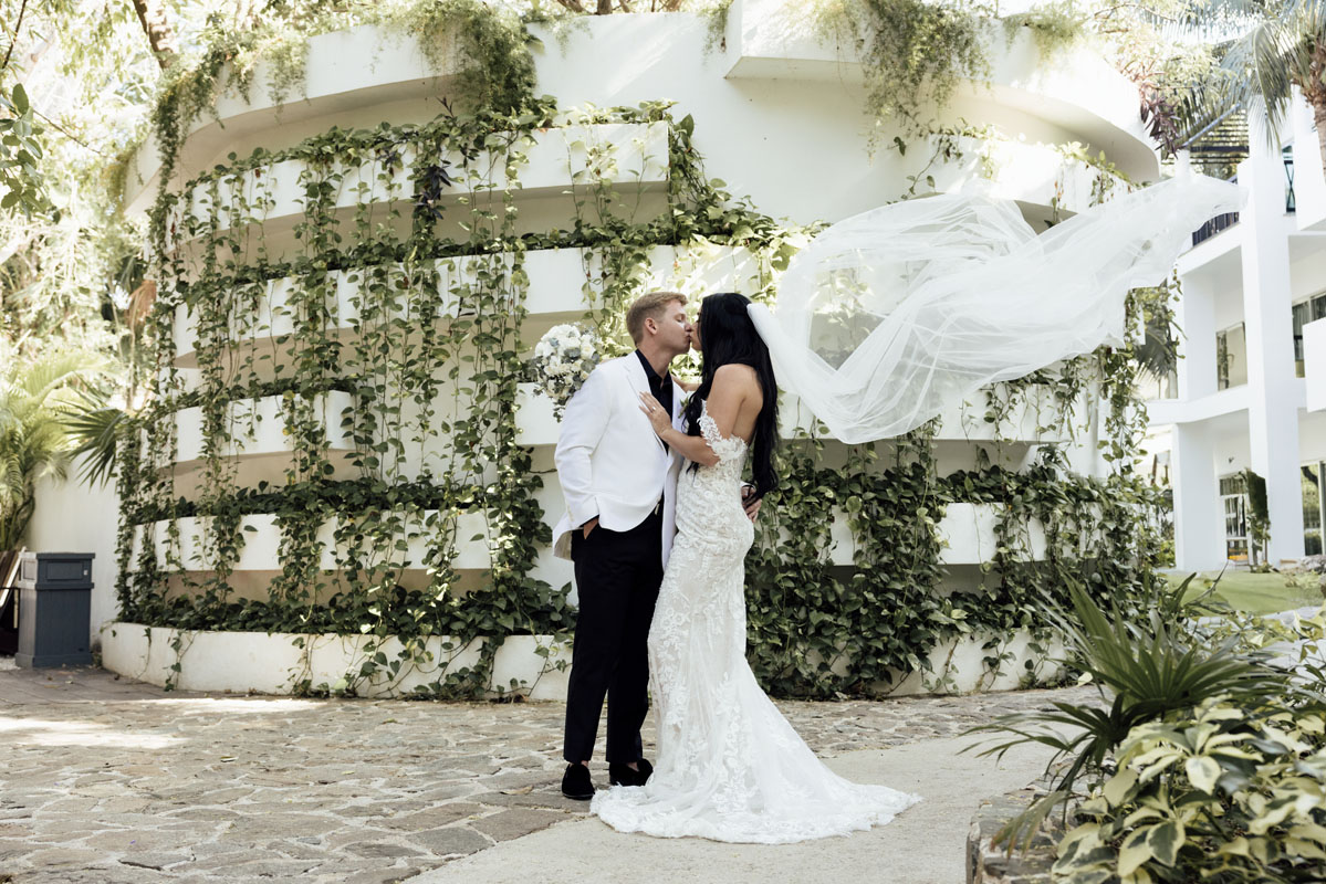 Newlyweds kiss on scenic path as brides veil billows on the breeze