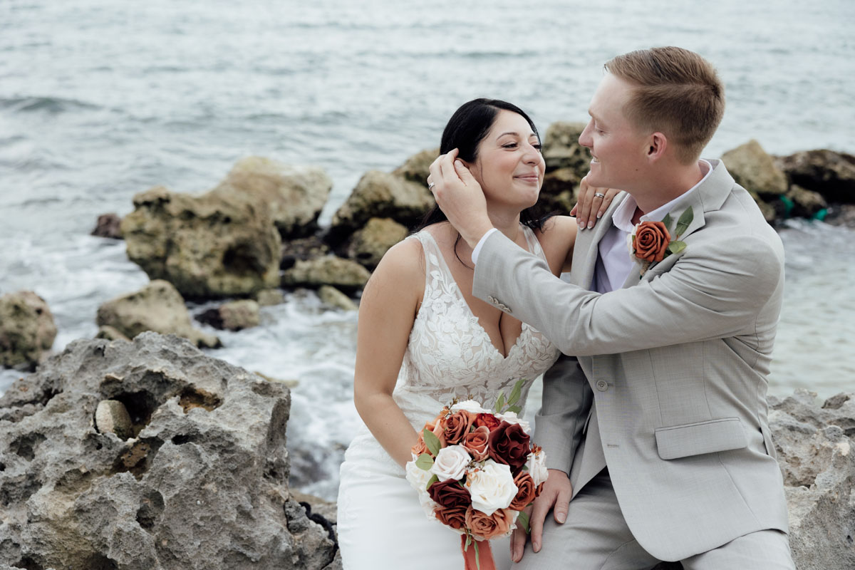 Newlyweds embrace sitting on rocky beach