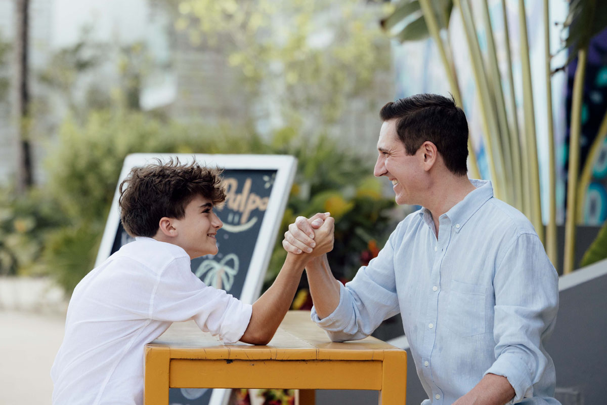 Father and son laugh arm wrestling each other