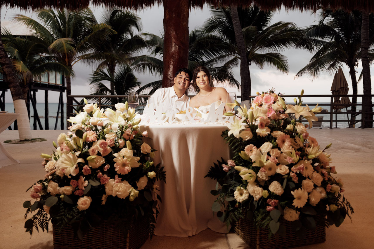 Newlyweds at head table surrounded by tropical flowers and swaying palms