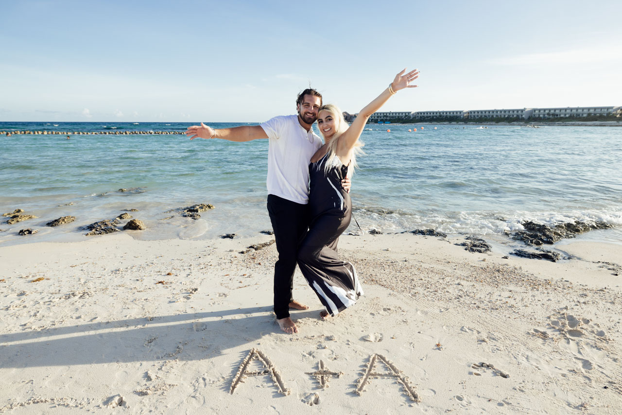 Newly engaged couple cheer on beach behind their initials in the sand
