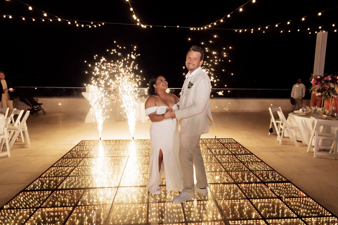 Newlyweds laugh together at their first dance framed by spouting fireworks
