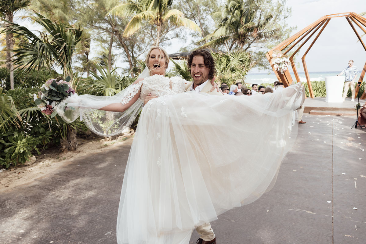 Groom lifts laughing bride in his arms after their ceremony