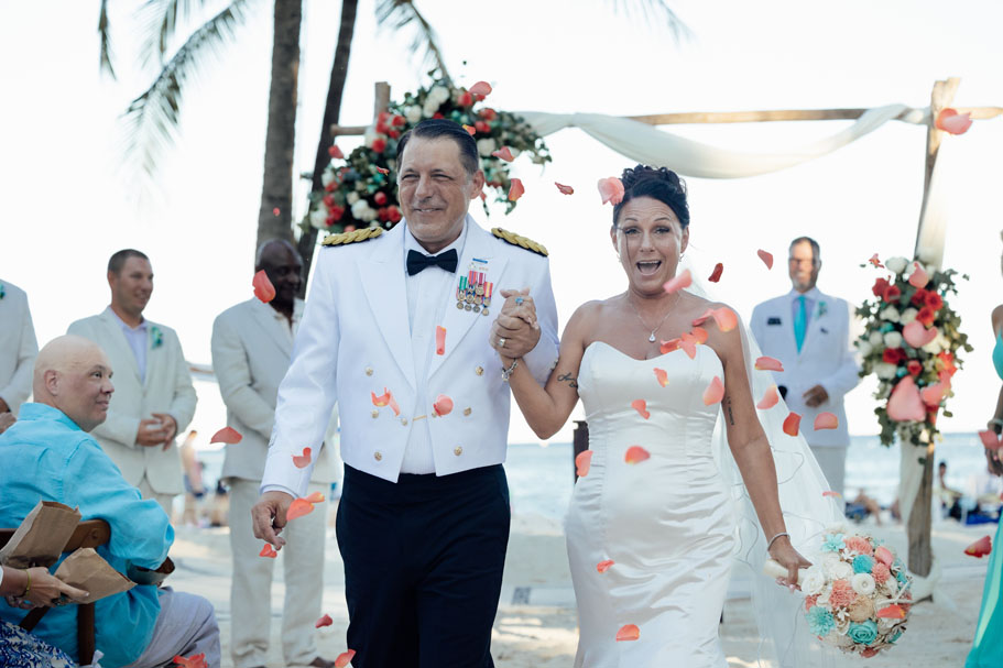 Smiling newlyweds walk out holding hands in a shower of petals