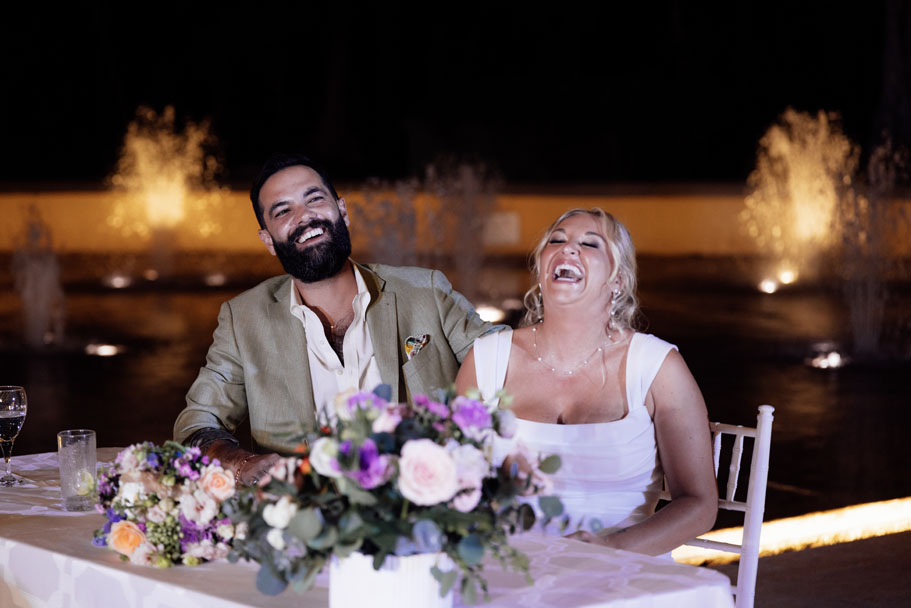 Newlyweds laugh, sitting at their reception head table