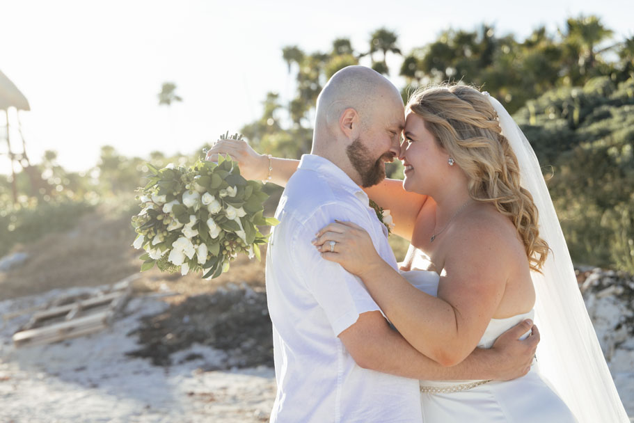 Newlyweds embrace on the beach, gazing into each others' eyes