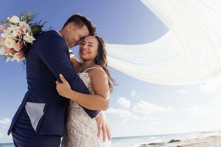 Smiling newlyweds embrace under the brides billowing veil